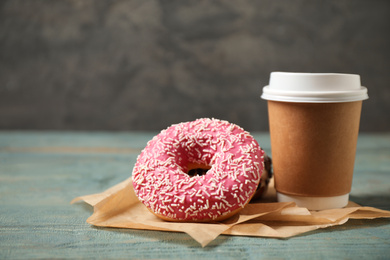 Photo of Yummy donuts with sprinkles and paper cup on wooden table