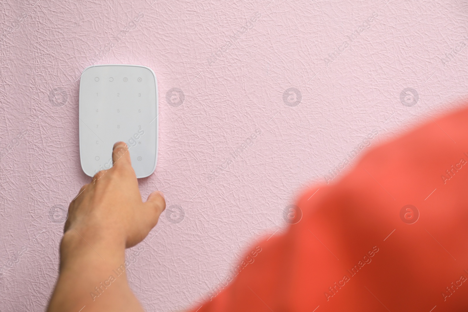 Photo of Young man entering code on alarm system keypad indoors