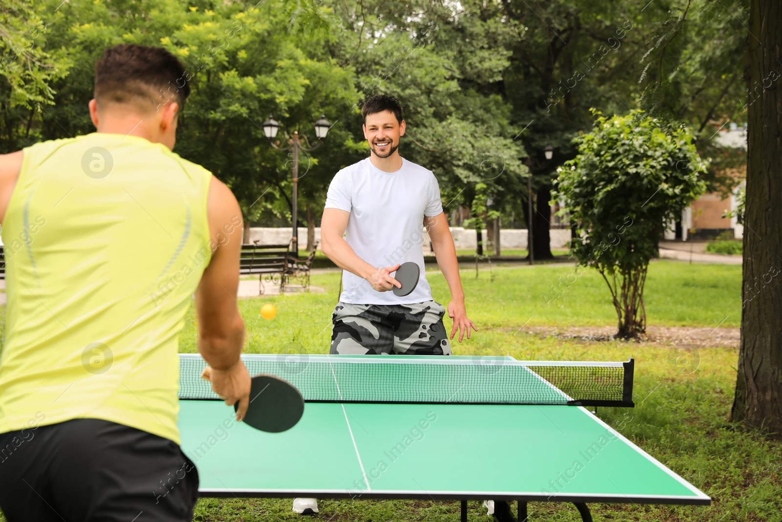Photo of Men playing ping pong in park on summer day