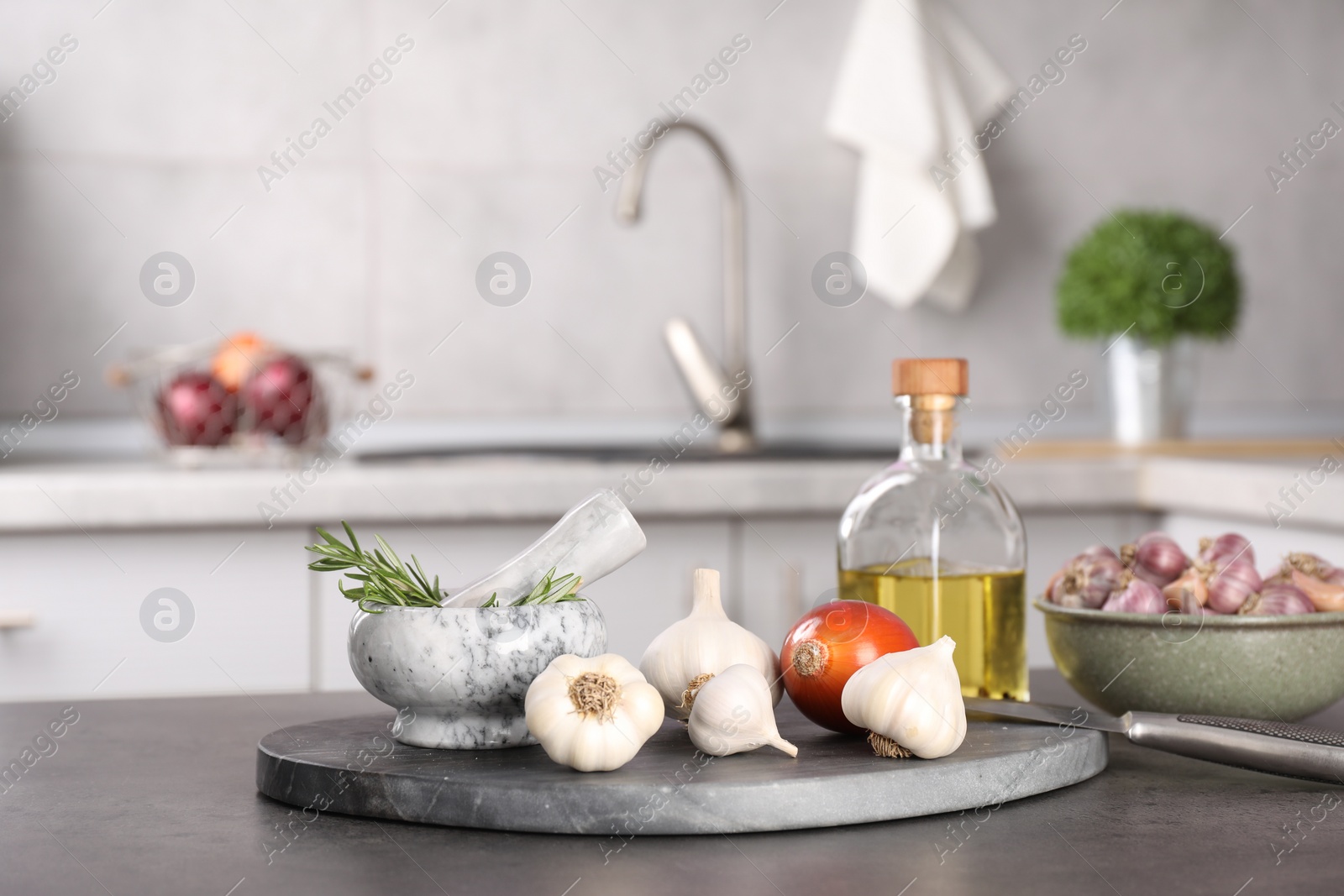 Photo of Fresh raw garlic, onion, rosemary and oil on grey table