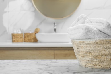 Photo of Wicker basket with folded bath towels on white marble table in bathroom, space for text