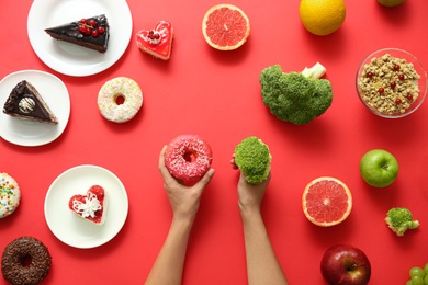Photo of Top view of woman choosing between sweets and healthy food on red background, closeup