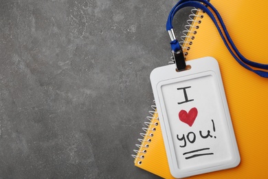 Photo of Badge with words I LOVE YOU and notebook on grey table, flat lay. Space for text