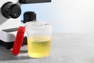 Photo of Container with urine sample for analysis and test strips on grey table in laboratory, space for text