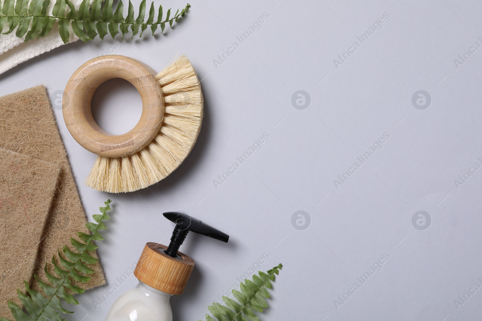 Photo of Cleaning brush, sponges, dispenser and fern leaves on grey background, flat lay. Space for text