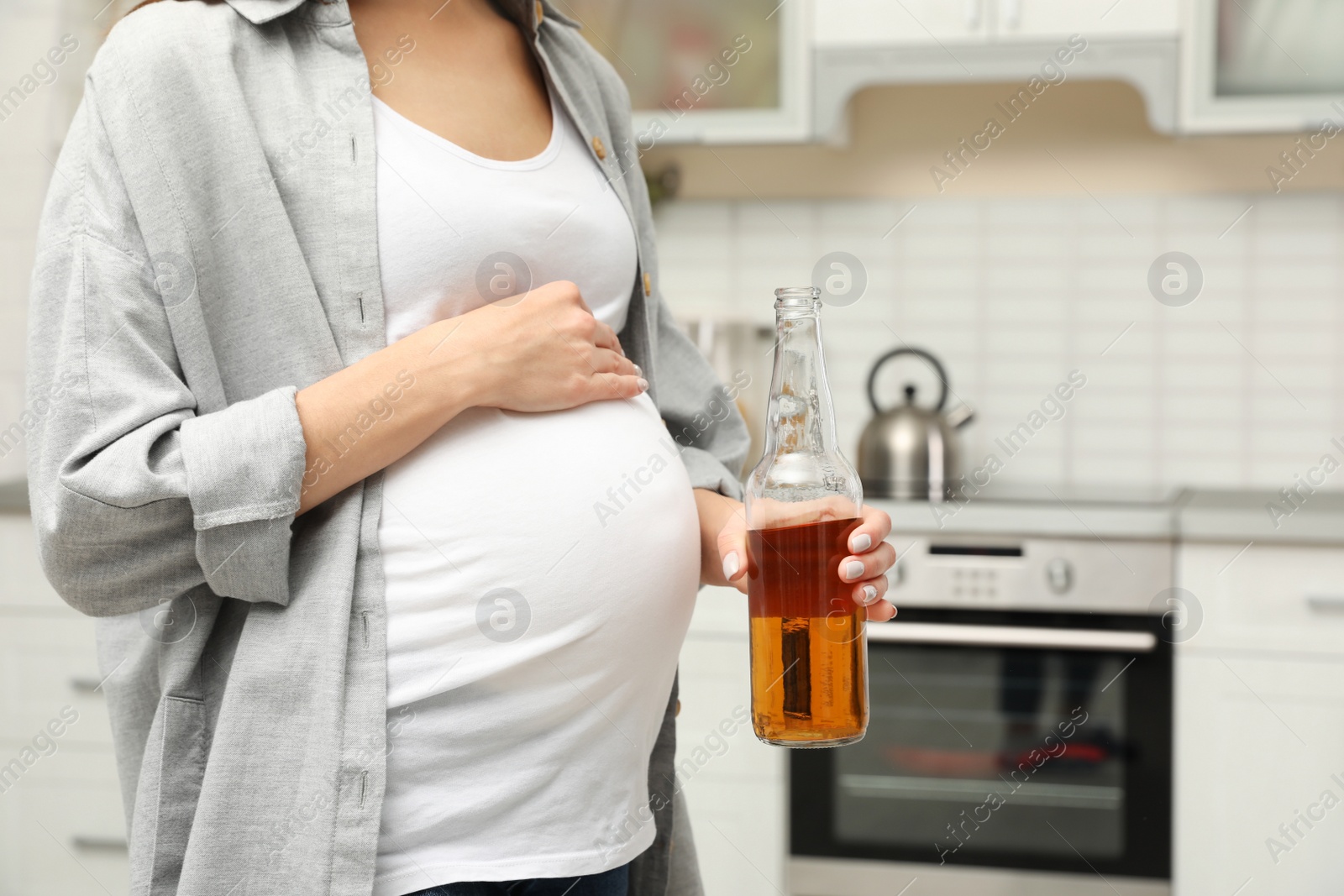 Photo of Future mother with bottle of alcohol drink in kitchen, closeup. Bad habits during pregnancy