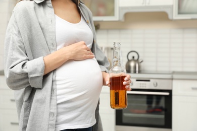 Photo of Future mother with bottle of alcohol drink in kitchen, closeup. Bad habits during pregnancy