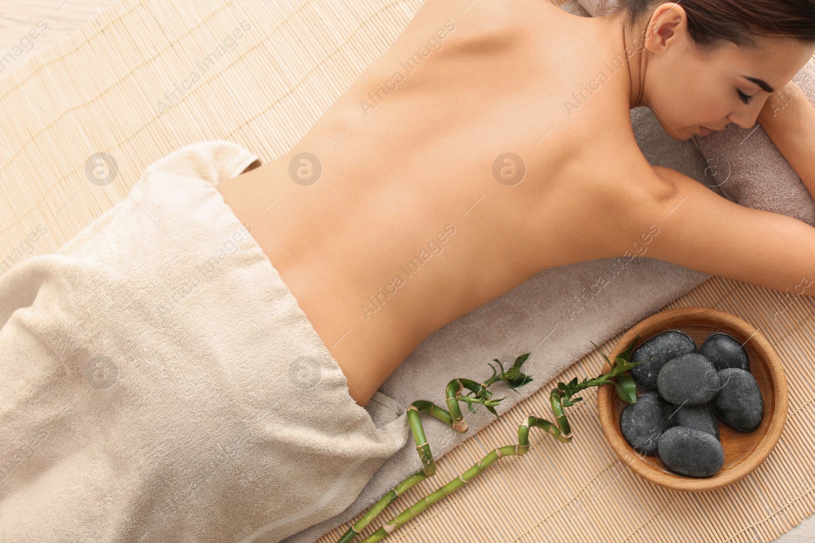 Photo of Beautiful young woman relaxing after massage on bamboo mat, top view