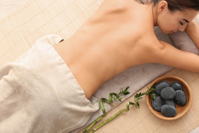 Beautiful young woman relaxing after massage on bamboo mat, top view