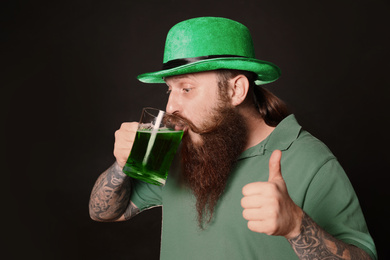 Photo of Bearded man drinking green beer on black background. St. Patrick's Day celebration