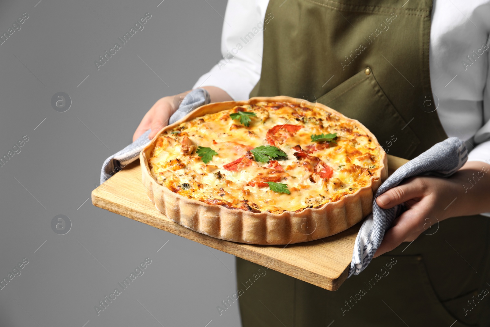 Photo of Woman holding board with tasty quiche on grey background, closeup
