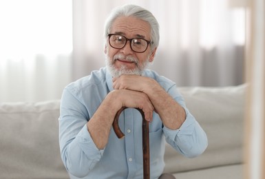 Photo of Portrait of grandpa with glasses and walking cane on sofa indoors