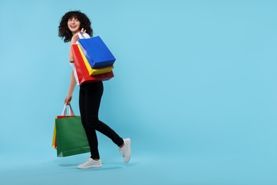 Photo of Happy young woman with shopping bags on light blue background. Space for text