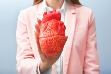 Photo of Woman holding model of heart on light background. Heart attack concept