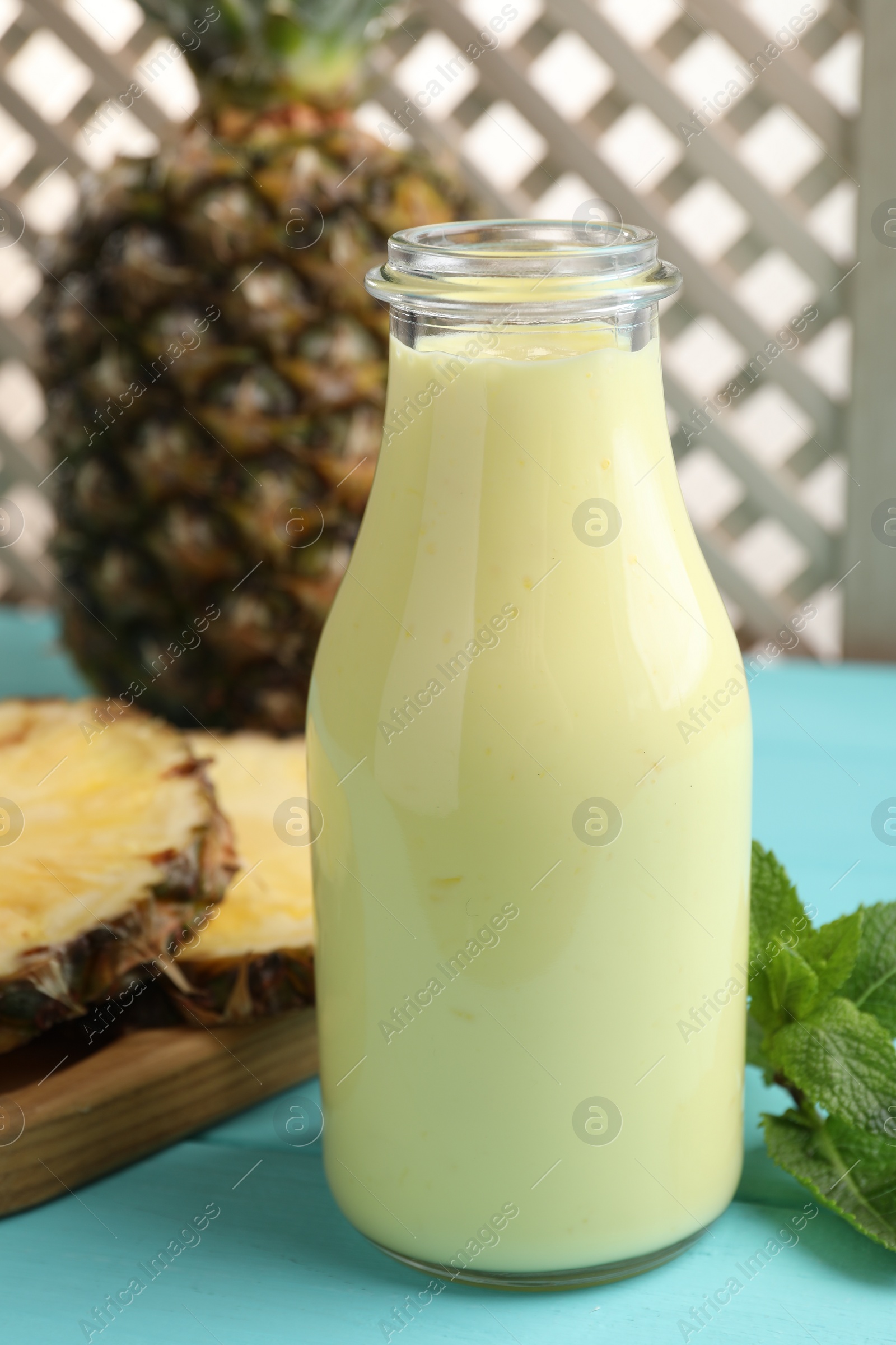 Photo of Tasty pineapple smoothie in bottle, mint and fruit on light blue wooden table