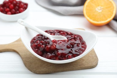 Photo of Fresh cranberry sauce in bowl and spoon on white wooden table, closeup