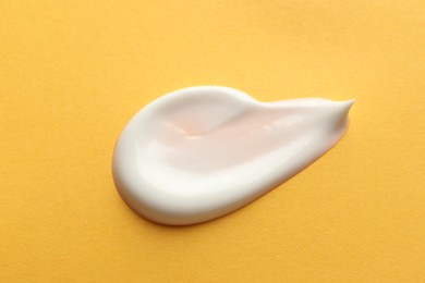 Sample of face cream on orange background, top view