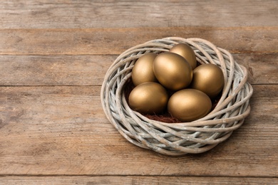 Golden eggs in nest on wooden background, space for text