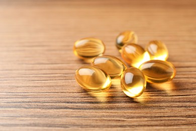 Photo of Dietary supplement capsules on wooden table, closeup. Space for text