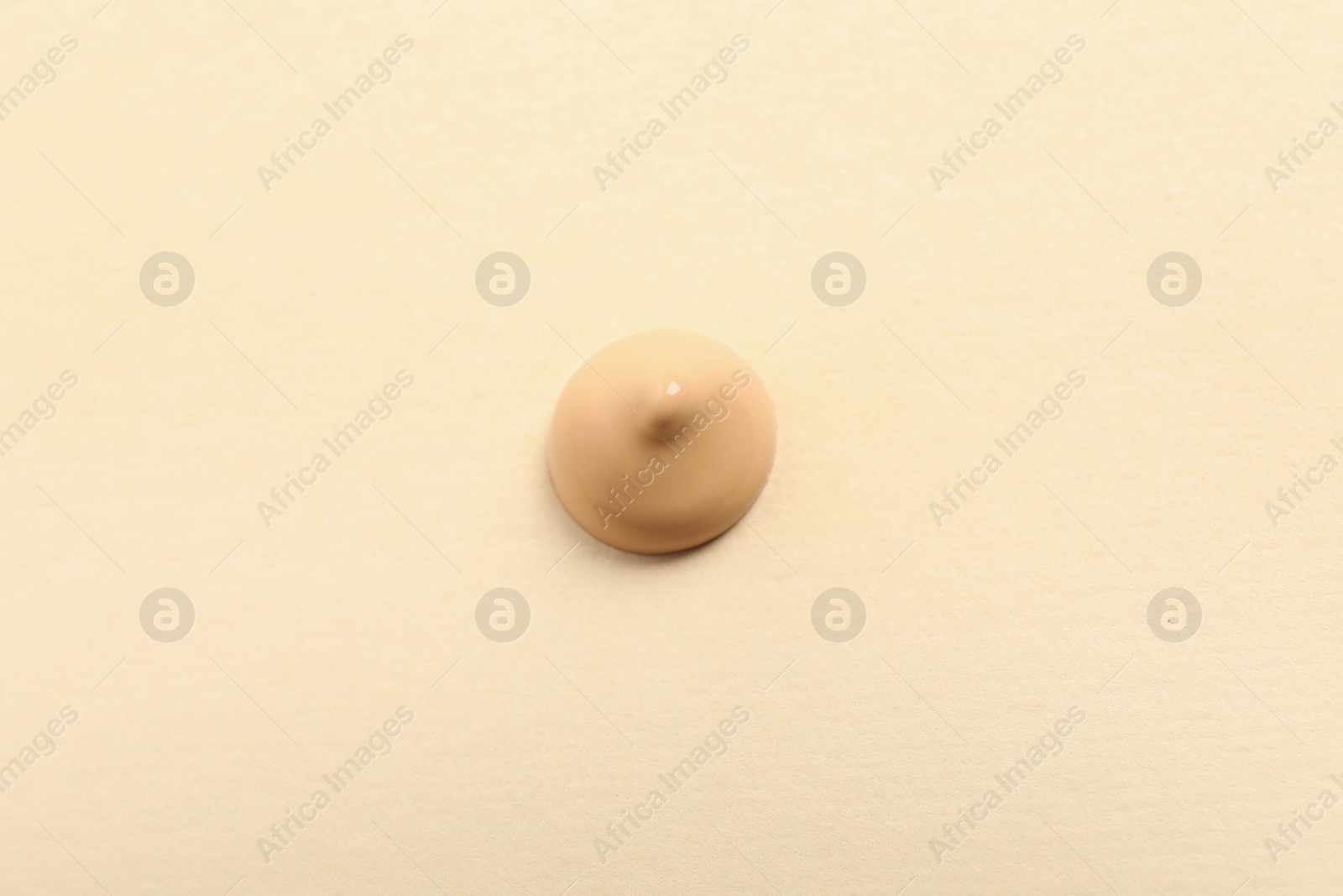 Photo of Drop of skin foundation on beige background, top view
