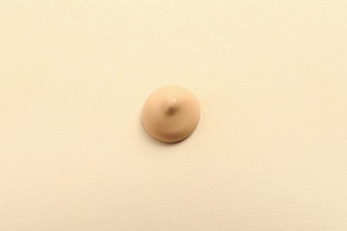 Drop of skin foundation on beige background, top view