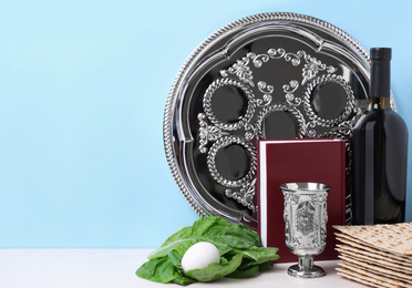 Photo of Symbolic Pesach (Passover Seder) items on white  table against light blue background, space for text