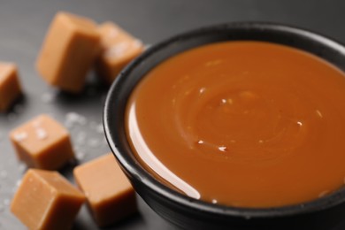 Photo of Yummy salted caramel in bowl and candies on black table, closeup