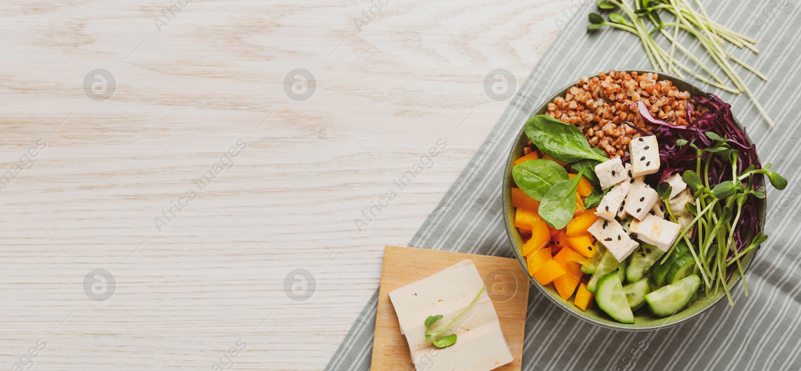 Image of Delicious vegan bowl with bell pepper, tofu and buckwheat on wooden table, top view. Banner design with space for text