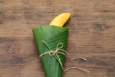 Photo of Delicious ripe banana wrapped in fresh leaf on wooden table, top view