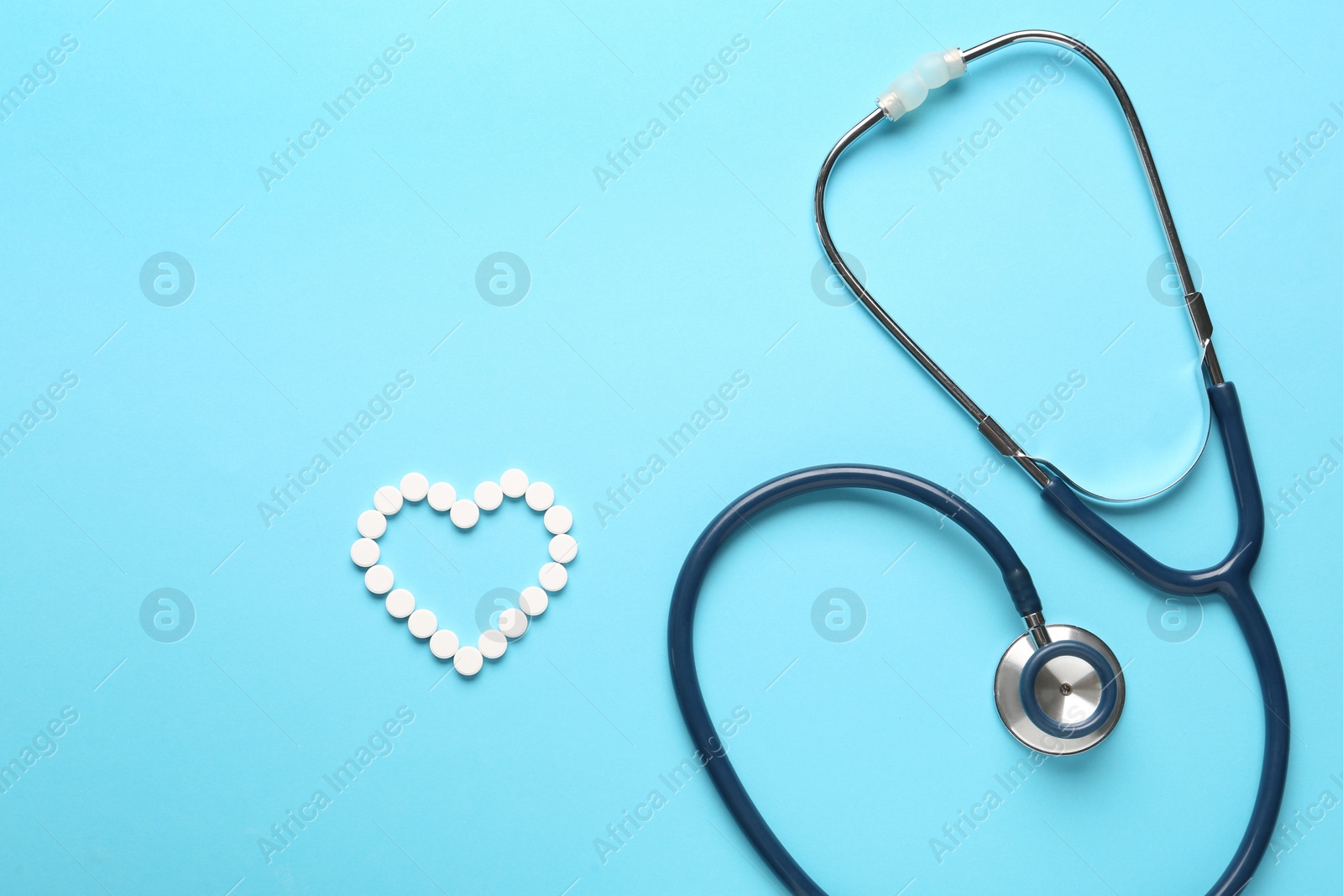 Photo of Flat lay composition with stethoscope and pills on light blue background