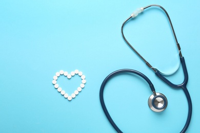 Flat lay composition with stethoscope and pills on light blue background