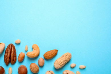 Different delicious nuts on light blue background, flat lay. Space for text