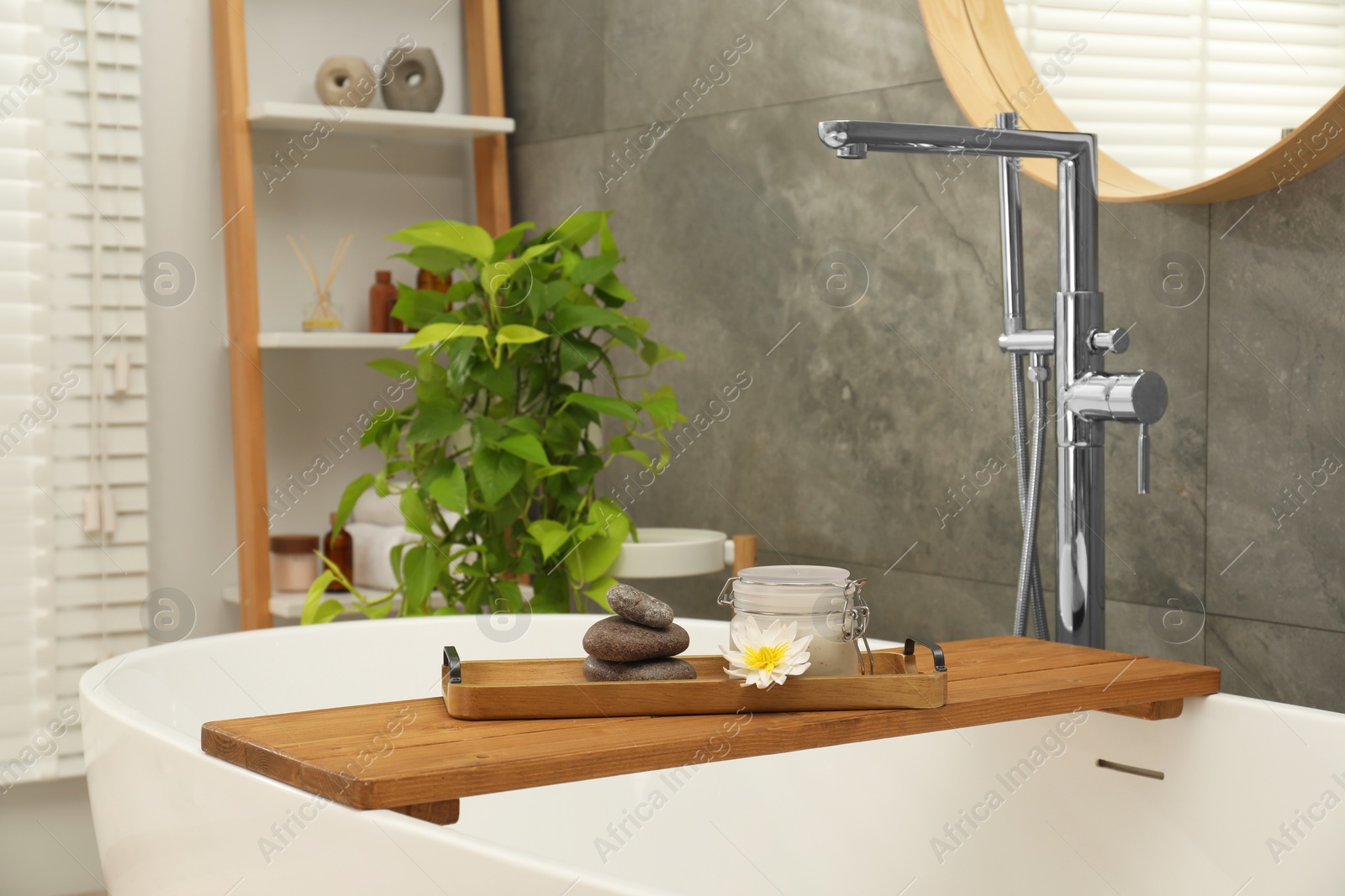 Photo of Shelving unit and wooden tub tray with different spa products in bathroom