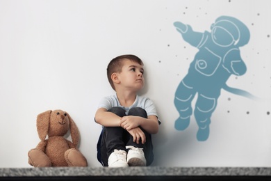 Little boy with soft toy dreaming to be spaceman. Silhouette of astronaut behind kid's back