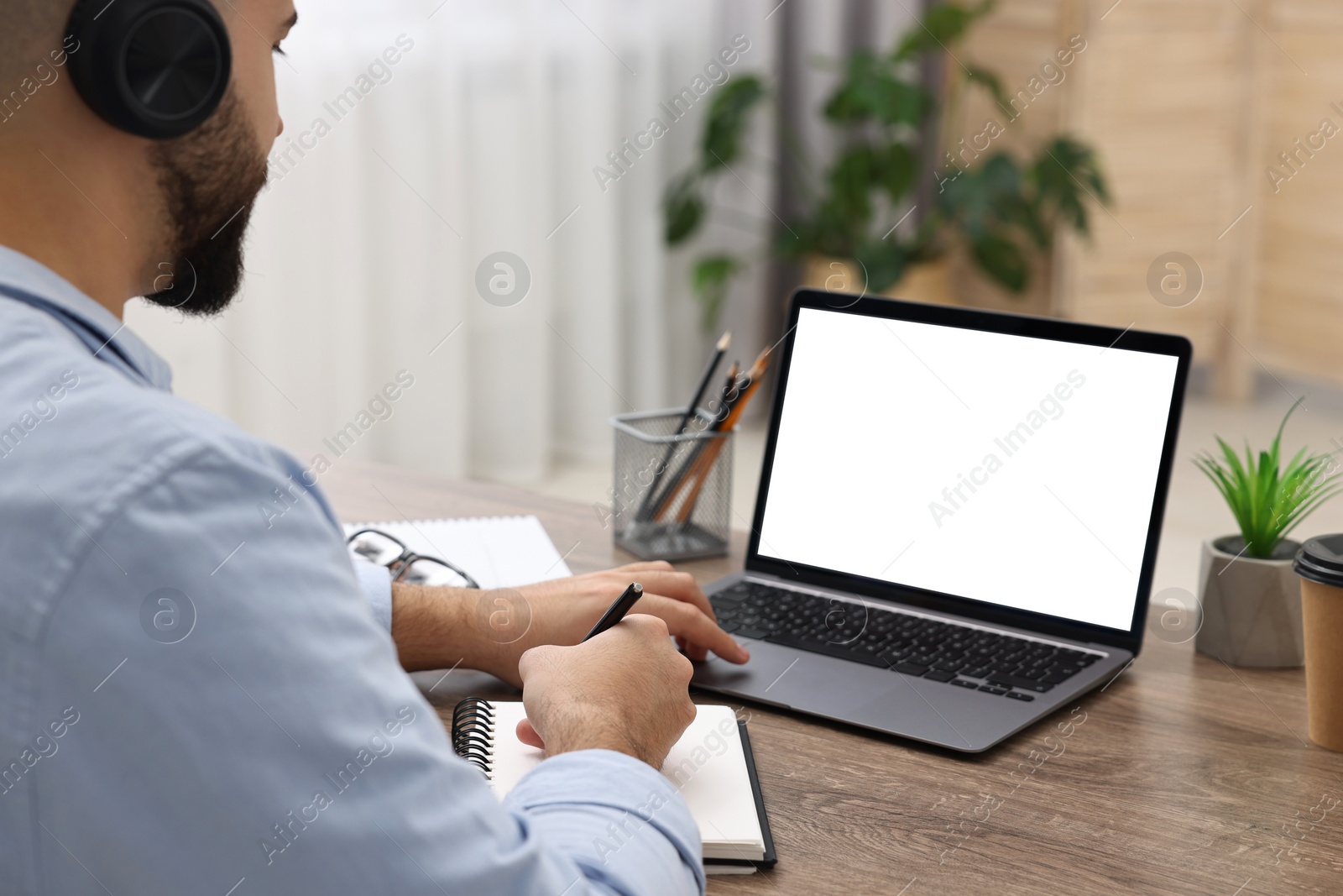 Photo of E-learning. Young man using laptop at wooden table indoors, closeup