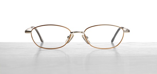 Stylish glasses with metal frame on table against white background