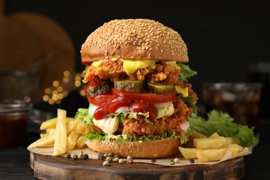 Photo of Delicious burger with crispy chicken patty and french fries on black wooden table, closeup