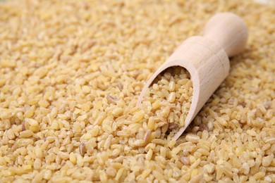 Photo of Wooden scoop and raw bulgur as background, closeup. Space for text