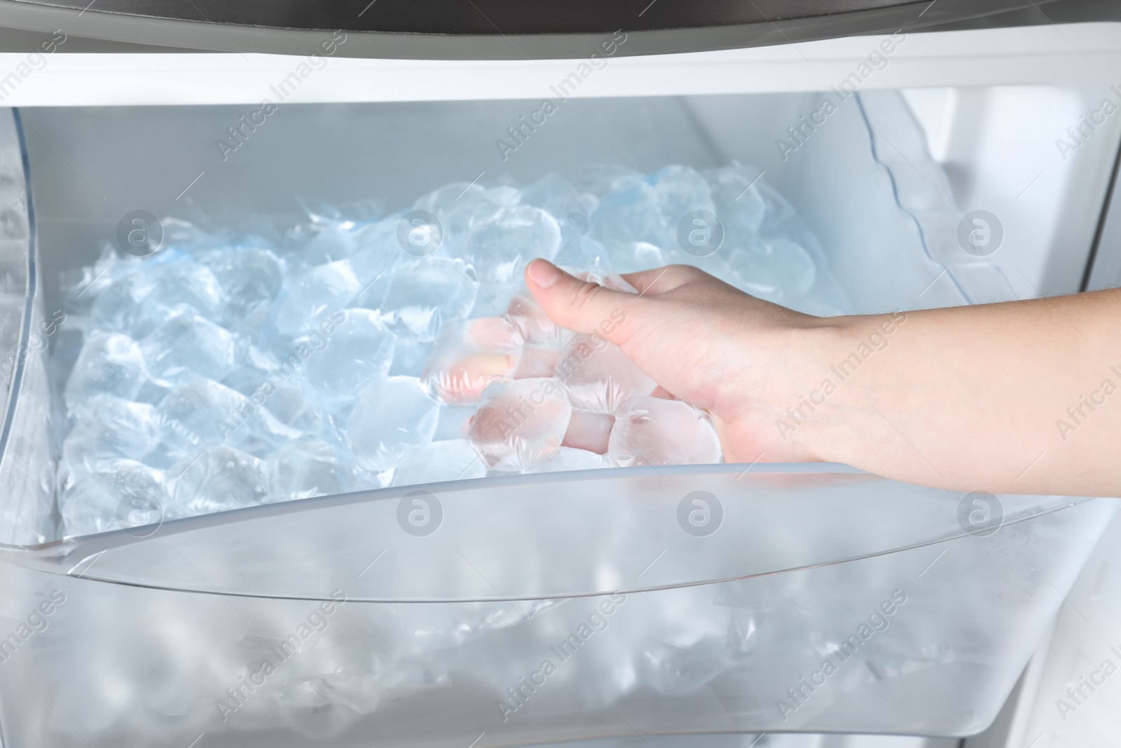 Photo of Woman taking plastic bag with ice cubes from fridge, closeup