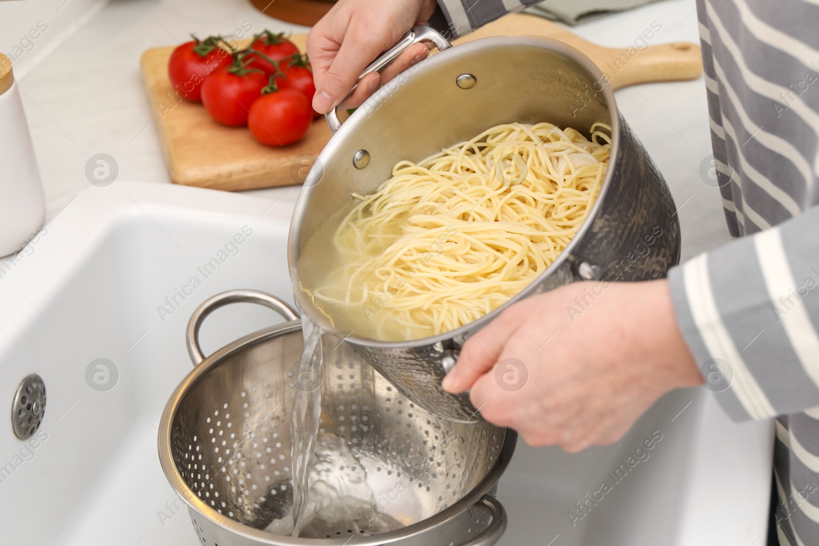 Photo of Woman draining pasta into colander at sink, closeup