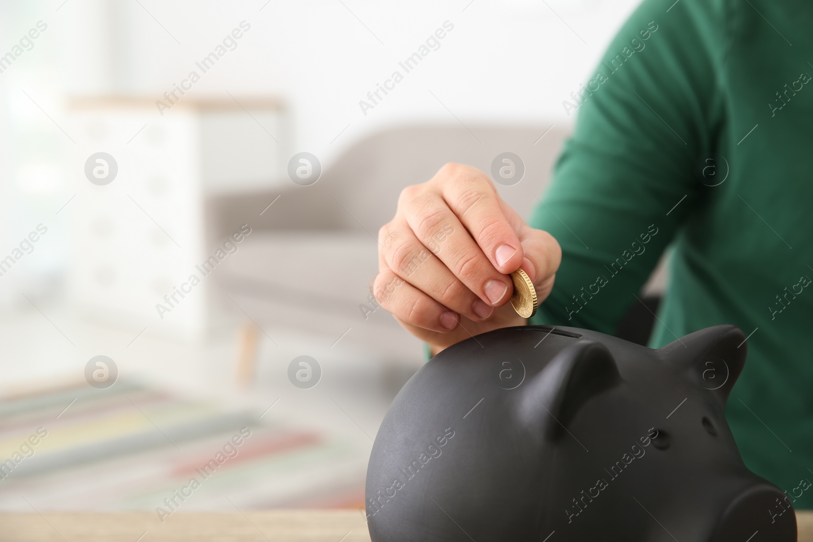Photo of Young man putting coin into piggy bank on blurred background, closeup with space for text