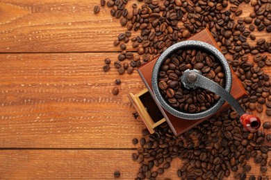 Photo of Vintage manual coffee grinder with beans on wooden table, flat lay. Space for text