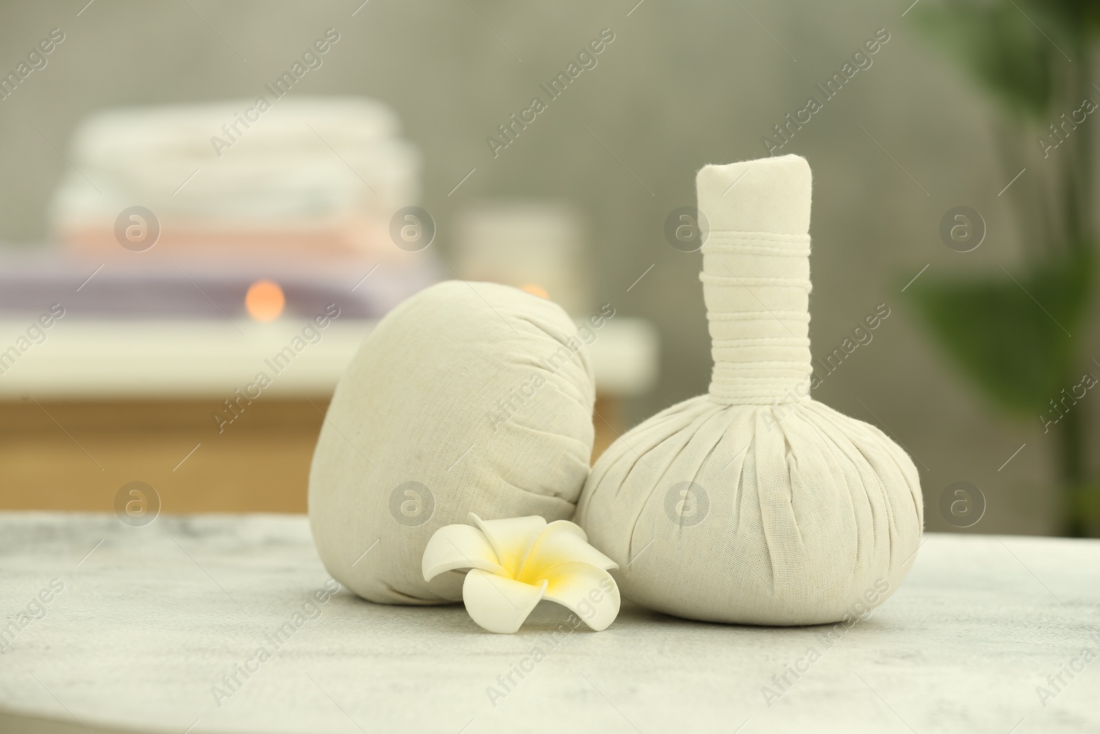 Photo of Beautiful spa composition with herbal massage bags and plumeria flower on light grey table in wellness center