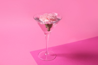 Martini glass with water and beautiful carnation flower on pink background