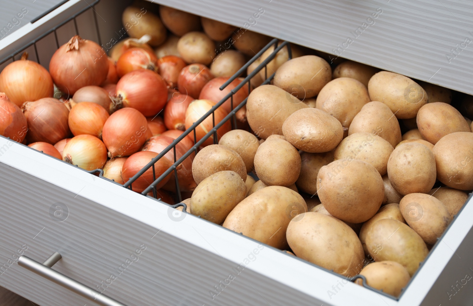 Photo of Open drawer with potatoes and onions in kitchen. Orderly storage