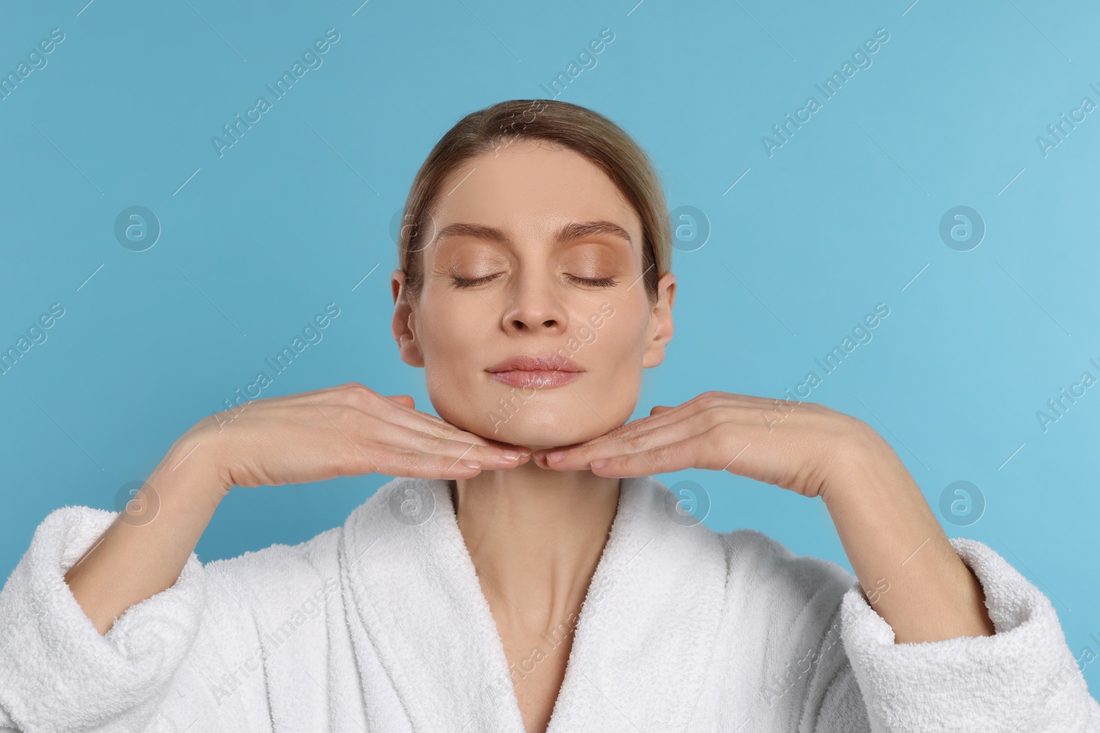 Photo of Woman massaging her face on turquoise background