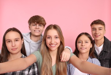 Photo of Group of happy teenagers taking selfie on pink background