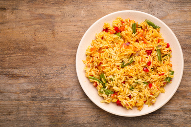 Photo of Tasty rice pilaf with vegetables on wooden table, top view. Space for text