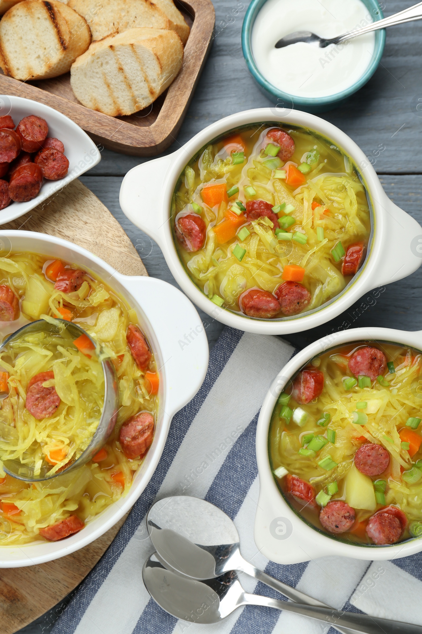 Photo of Delicious sauerkraut soup with smoked sausages and green onion served on grey wooden table, flat lay