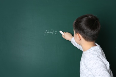 Child writing math sum on chalkboard. Space for text